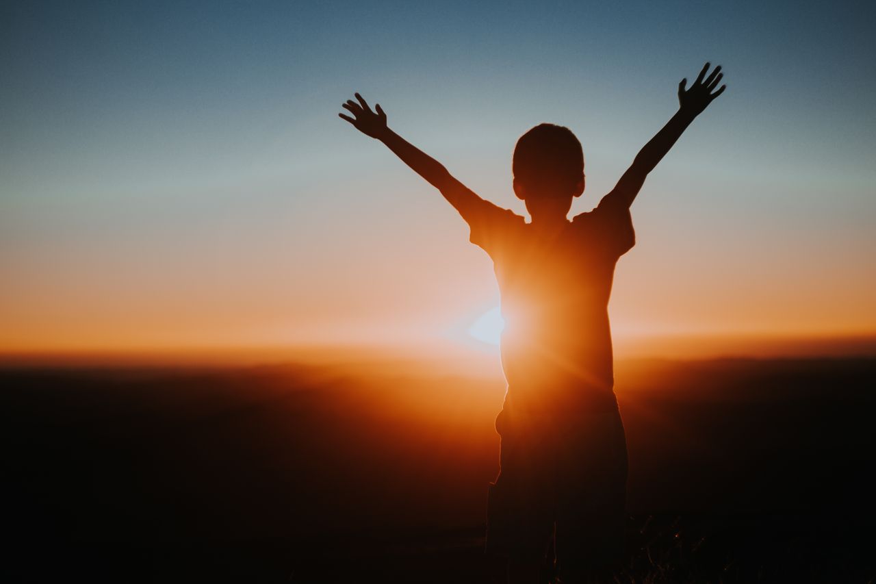 Services A child silhouette with raised arms enjoying a vibrant sunset, symbolizing freedom and joy.