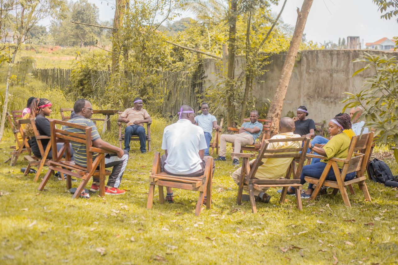 About A diverse group of adults gathered outdoors for a meeting on a sunny day in a peaceful garden setting.