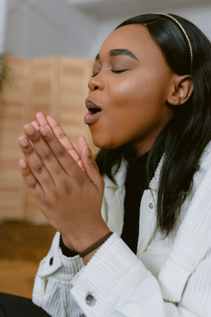 Home A young woman in deep prayer with eyes closed, conveying devotion and faith indoors.